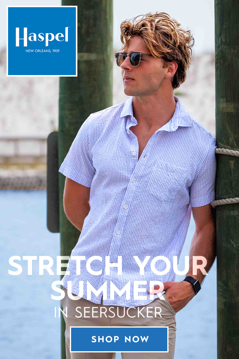 A stands on a dock by the water wearing a light blue button-up seersucker shirt and khaki pants, with large wooden posts framing the scene. White text across the center reads 'STRETCH YOUR SUMMER IN SEESUCKER' with a blue 'SHOP NOW' button below.