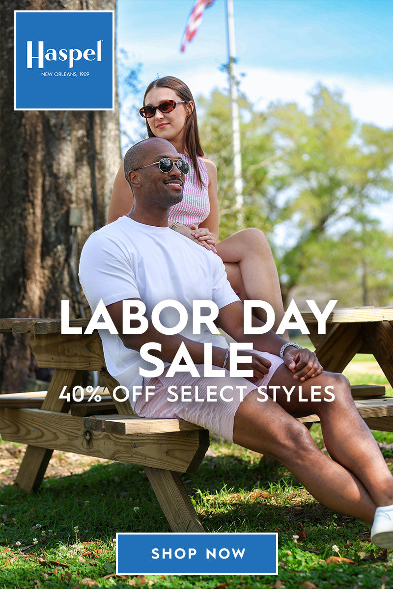 Outdoor lifestyle advertisement featuring a man and woman sitting on wooden picnic benches in a park, with large text reading 'LABOR DAY SALE 40% OFF SELECT STYLES' and a blue Haspel logo and 'SHOP NOW' button.