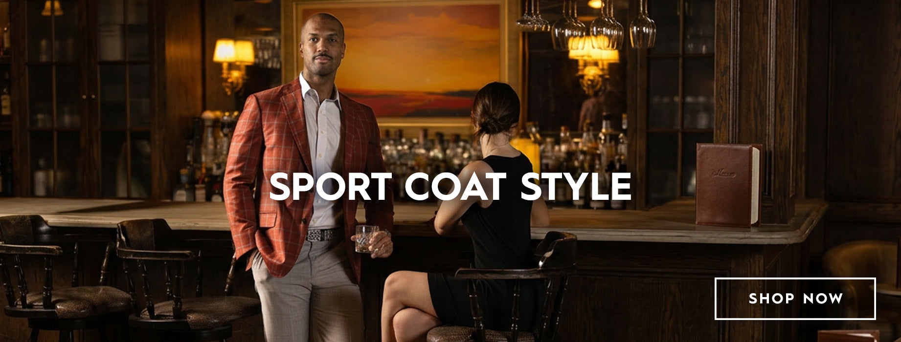 A man in a red windowpane sport coat and light grey trousers stands in a dimly lit bar setting, with a woman seated at the counter. Large text across the center reads 'SPORT COAT STYLE' and a 'SHOP NOW' box appears in the lower right corner.