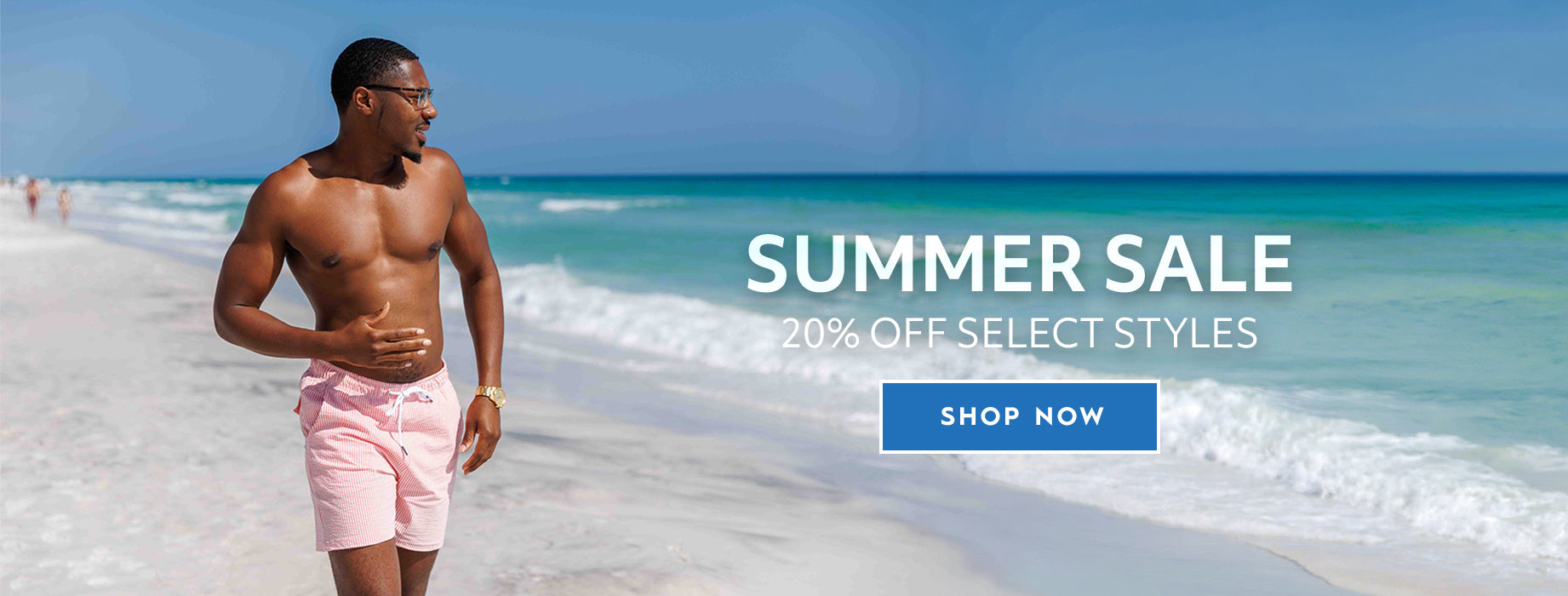 A shirtless man wearing coral seersucker swim trunks walks along a sandy beach with turquoise ocean water and a blue sky. Large text on the right reads 'SUMMER SALE 20% OFF SELECT STYLES' with a blue 'SHOP NOW' button below.