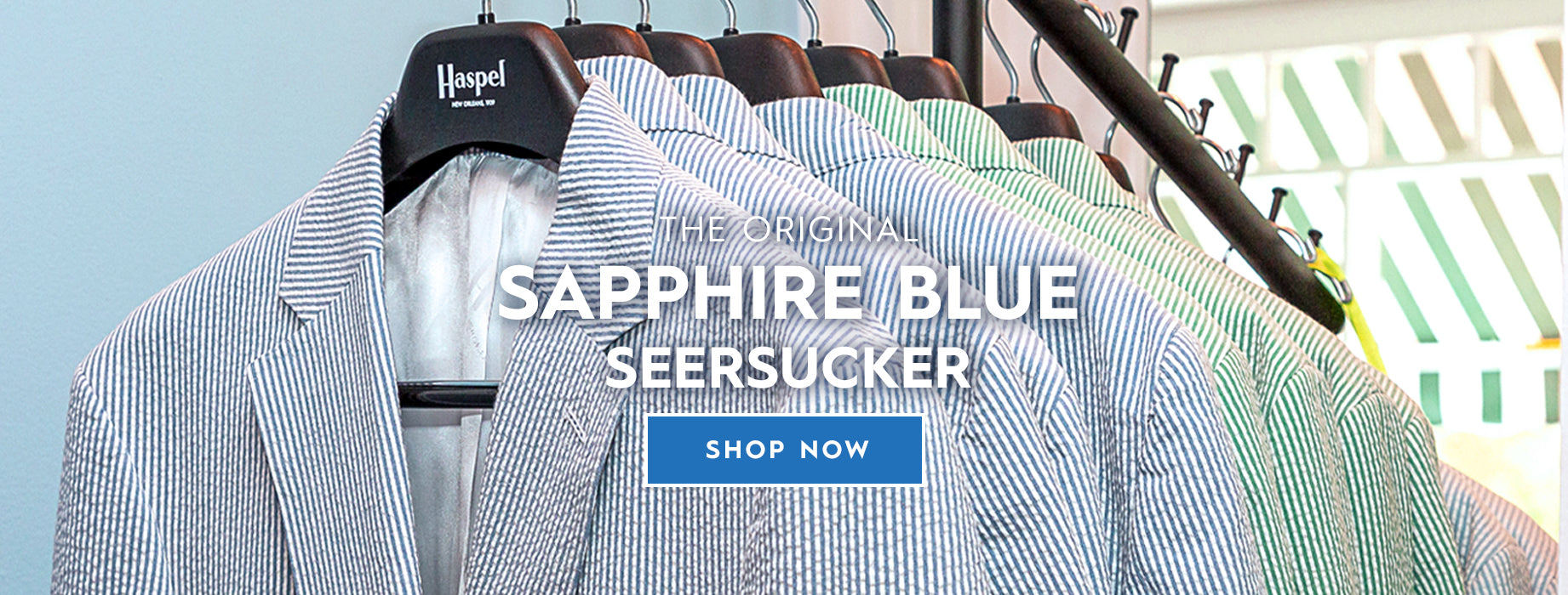 A close-up of a striped seersucker blazer on a clothing rack, with overlaid text reading 'The Original Sapphire Blue Seersucker' and a blue 'Shop Now' button.